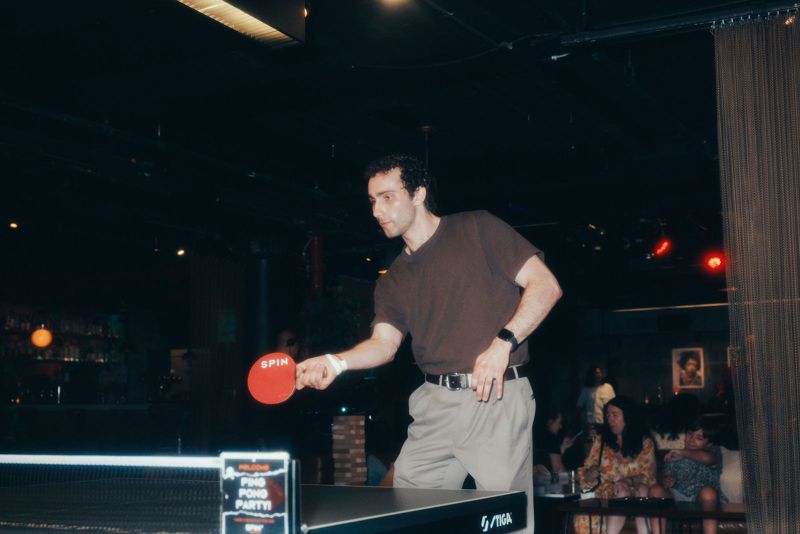 Guest in a brown shirt returning a shot