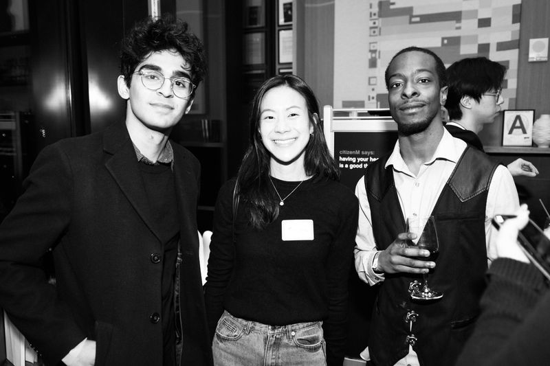 Three guests posing beside a wall sign, in black and white